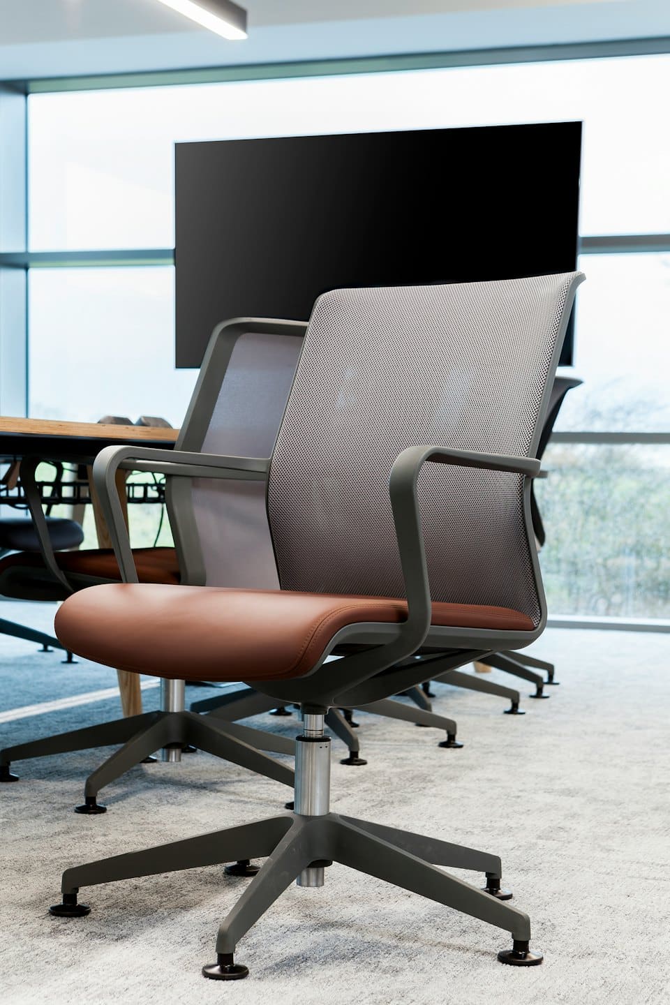 Ergonomic chairs are arranged around a wooden table in a boardroom.